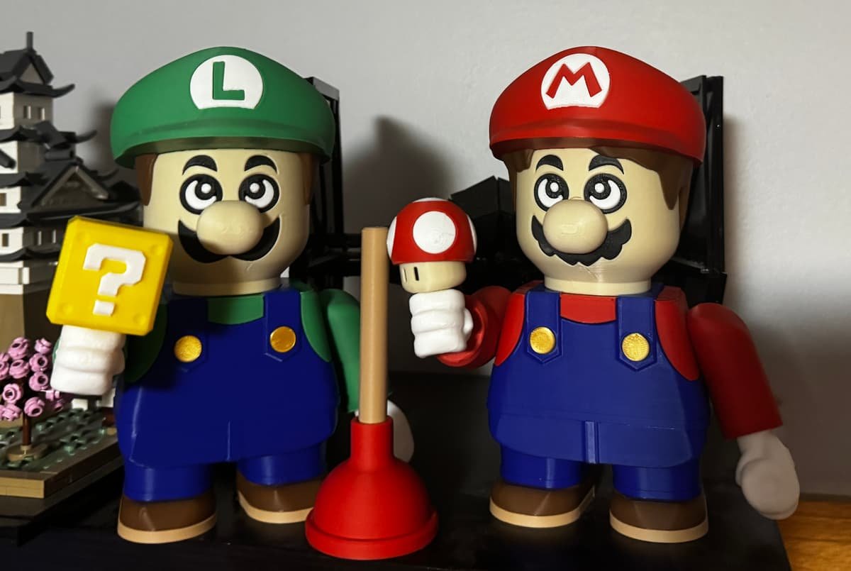 Mario e Luigi em estilo robusto impressos em 3D e coloridos, segurando cogumelo e bloco de interrogação