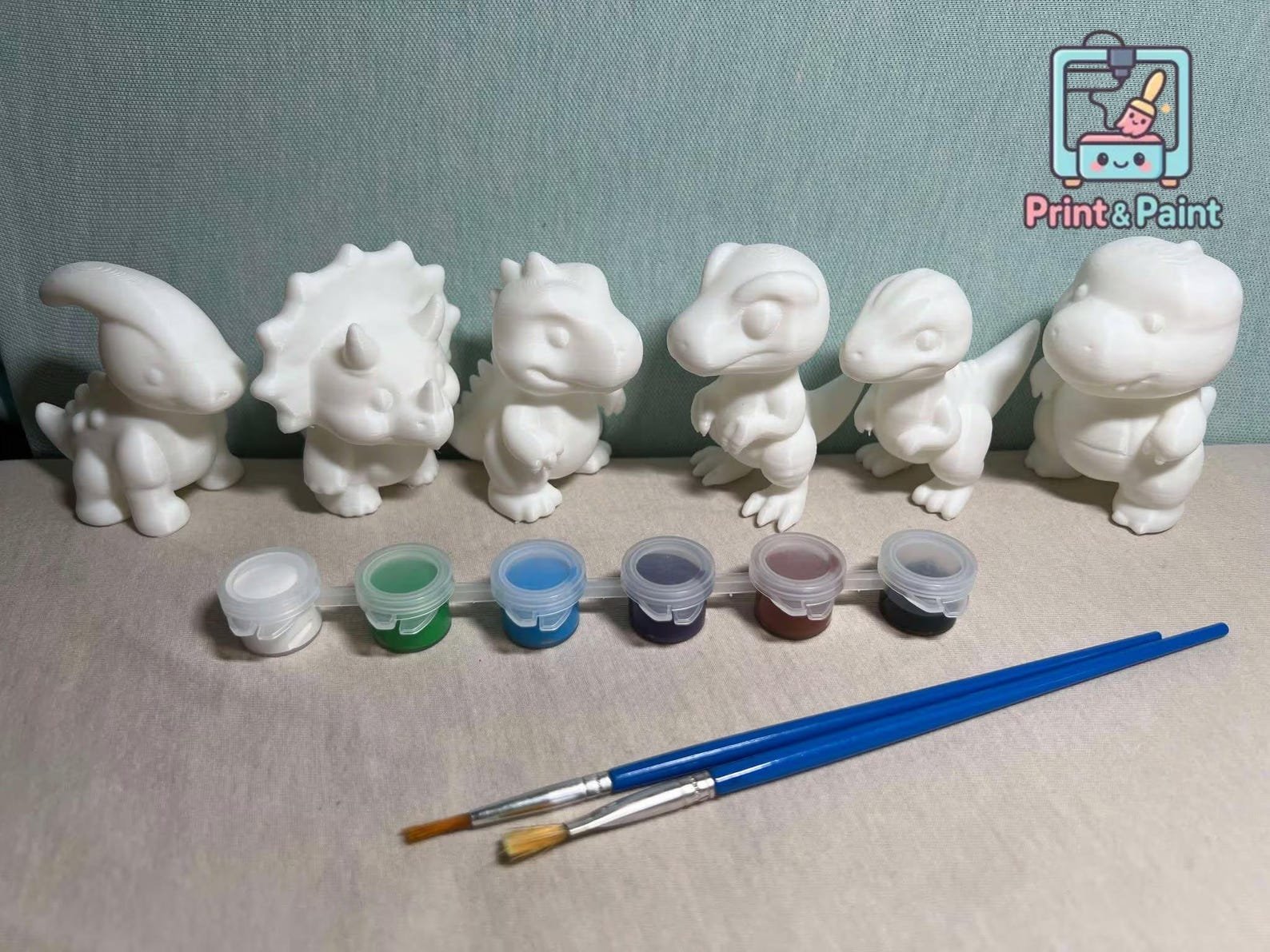 Dinossauros brancos impressos em 3D com potes de tintas e pincéis para colorir