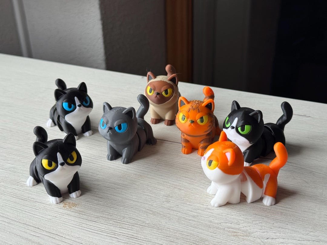 Coleção de gatos articulados coloridos impressos em 3D sobre uma mesa